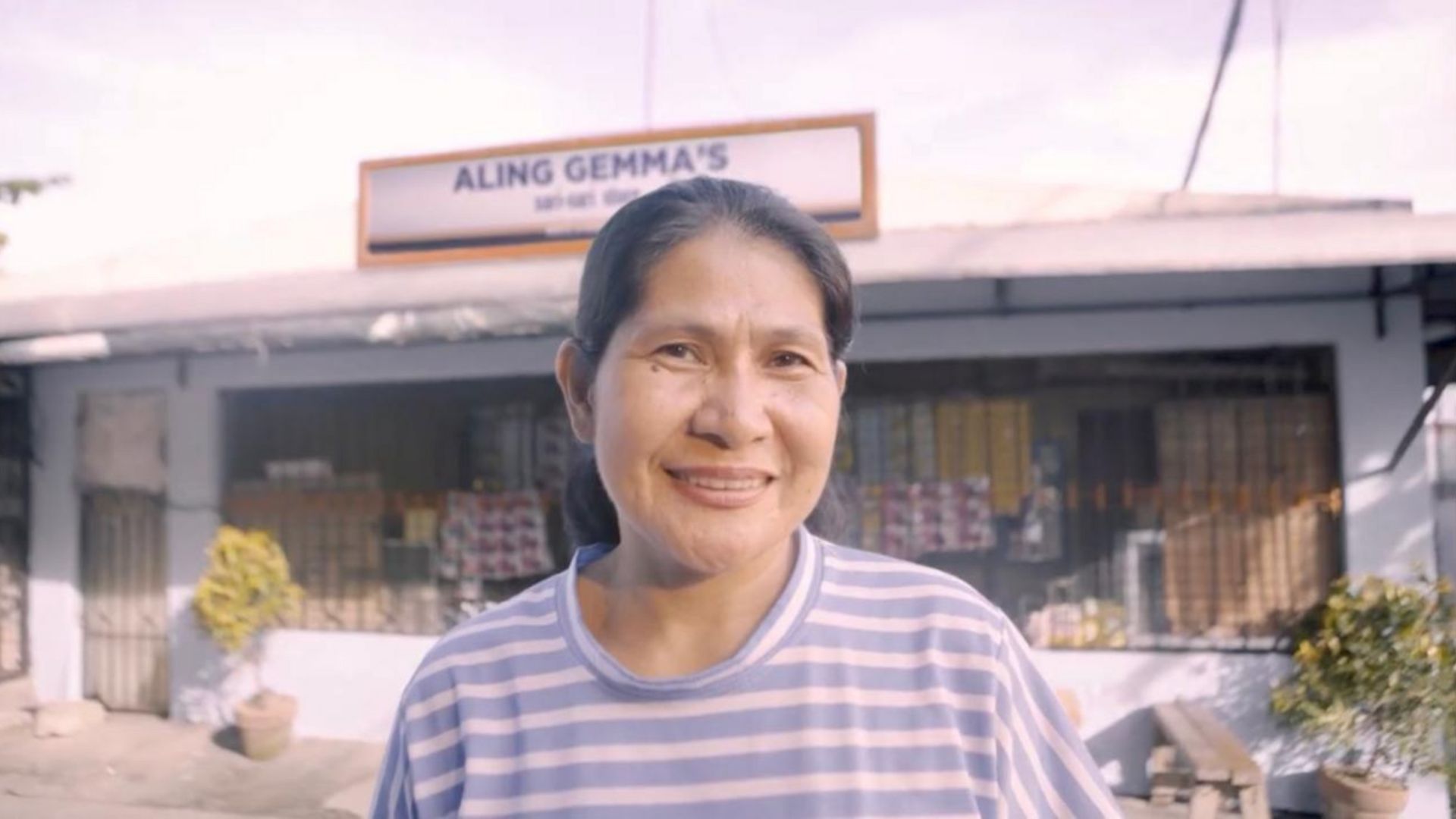A female sari-sari store owner standing in front of her store
