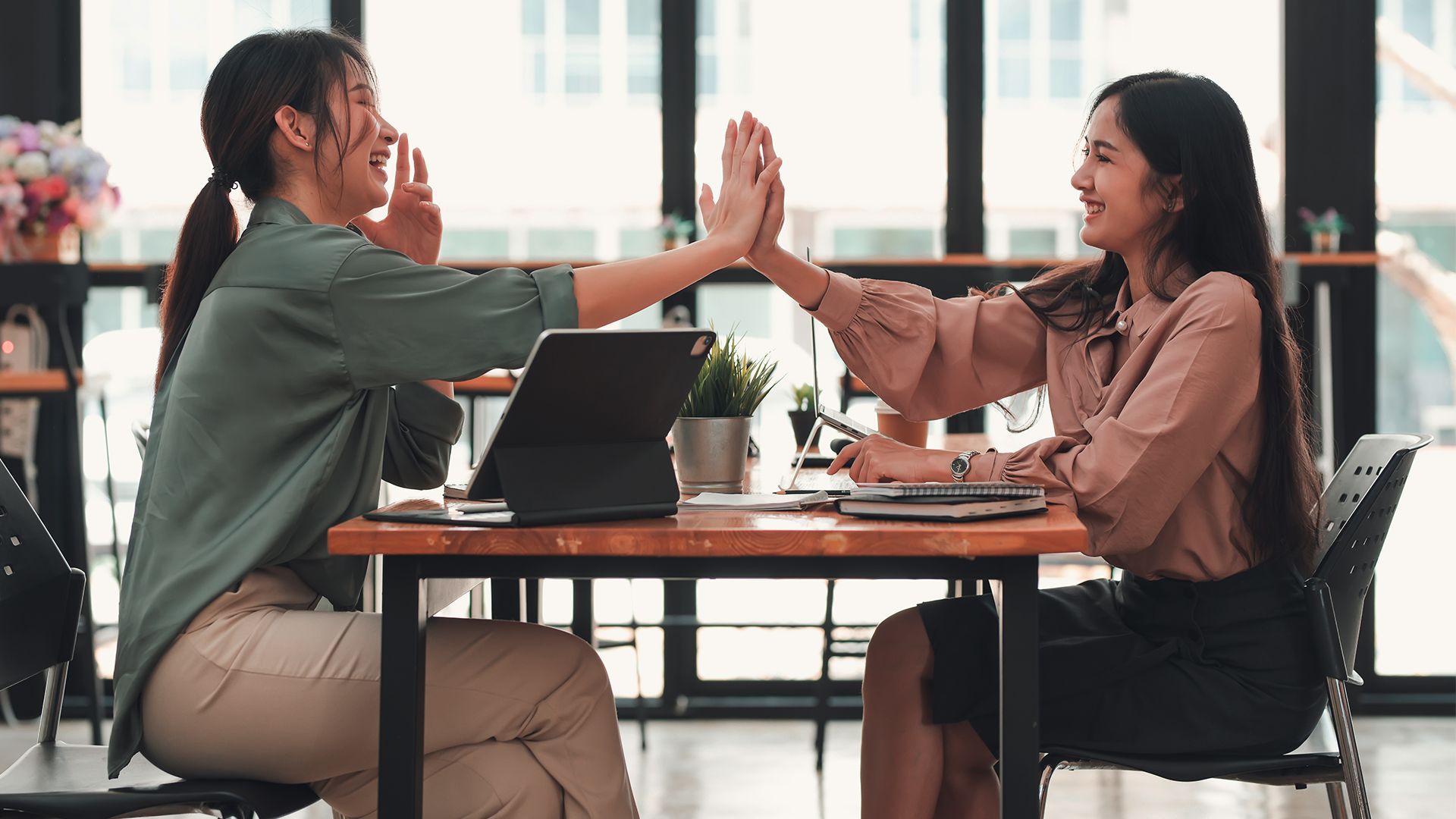 Two workers sitting at a table giving each other a high five