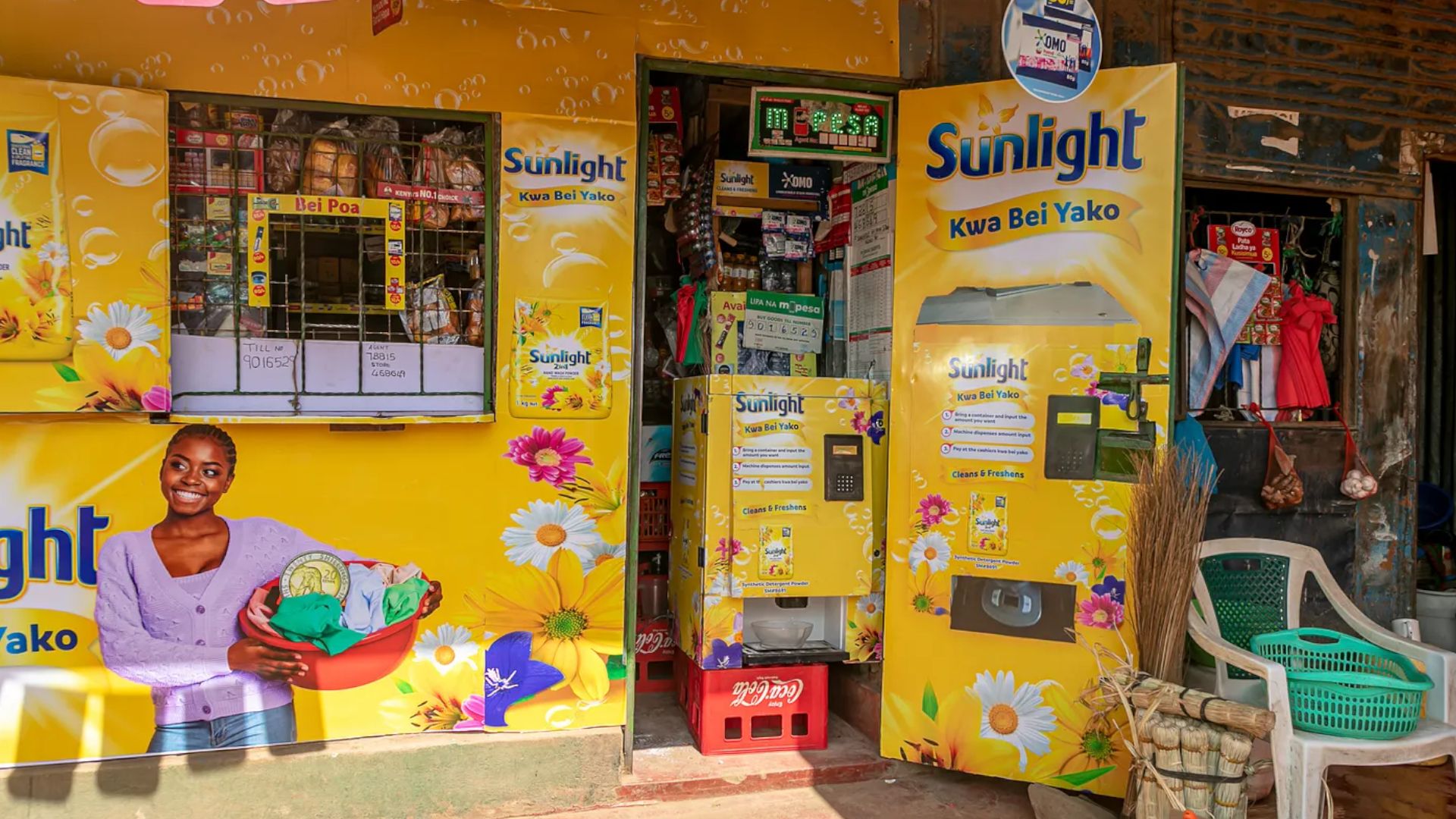 A small storefront featuring bright yellow branding for ‘Sunlight’ laundry detergent. The store includes a detergent vending machine and a small service counter, and is adorned with colourful illustrations of flowers.
