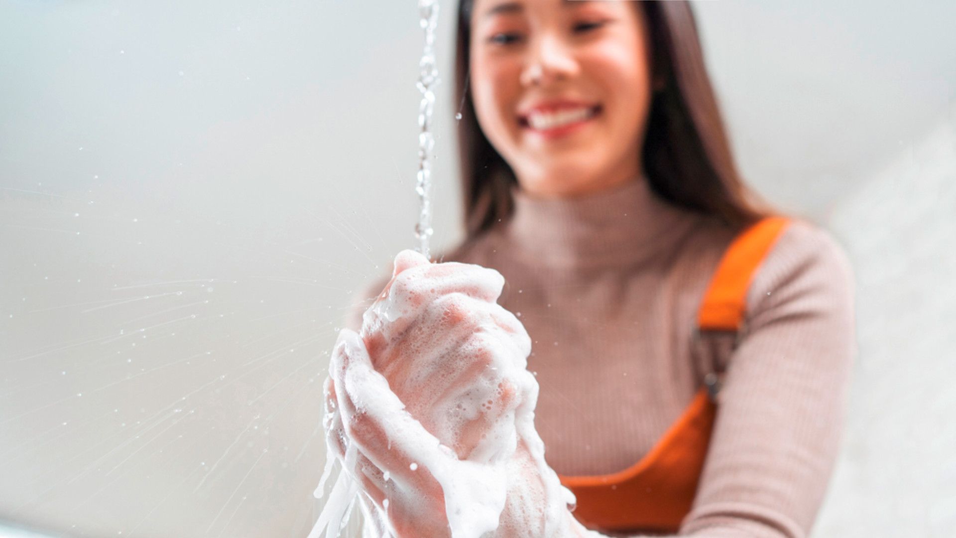 A happy woman washing her hands in the kitchen with soap.