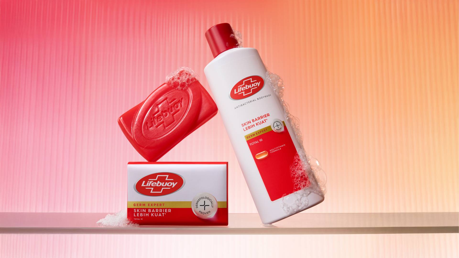 New red Lifebuoy soap bar and a new Lifebuoy body wash in a white, red and gold bottle. Background is pink and orange.