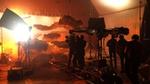 A film crew in a studio is setting up a shot of a large screen with floating grey and orange cut-out clouds.