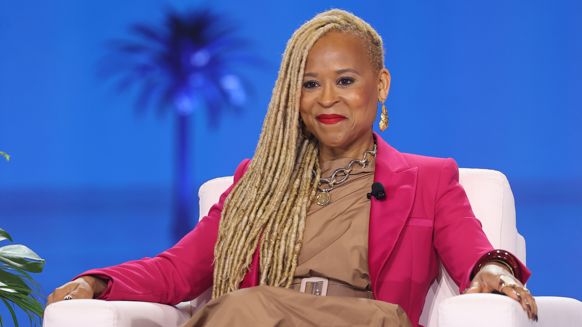 Portrait of Esi Eggleston Bracey, a woman with braided hair, wearing a brown dress and a bright pink jacket.