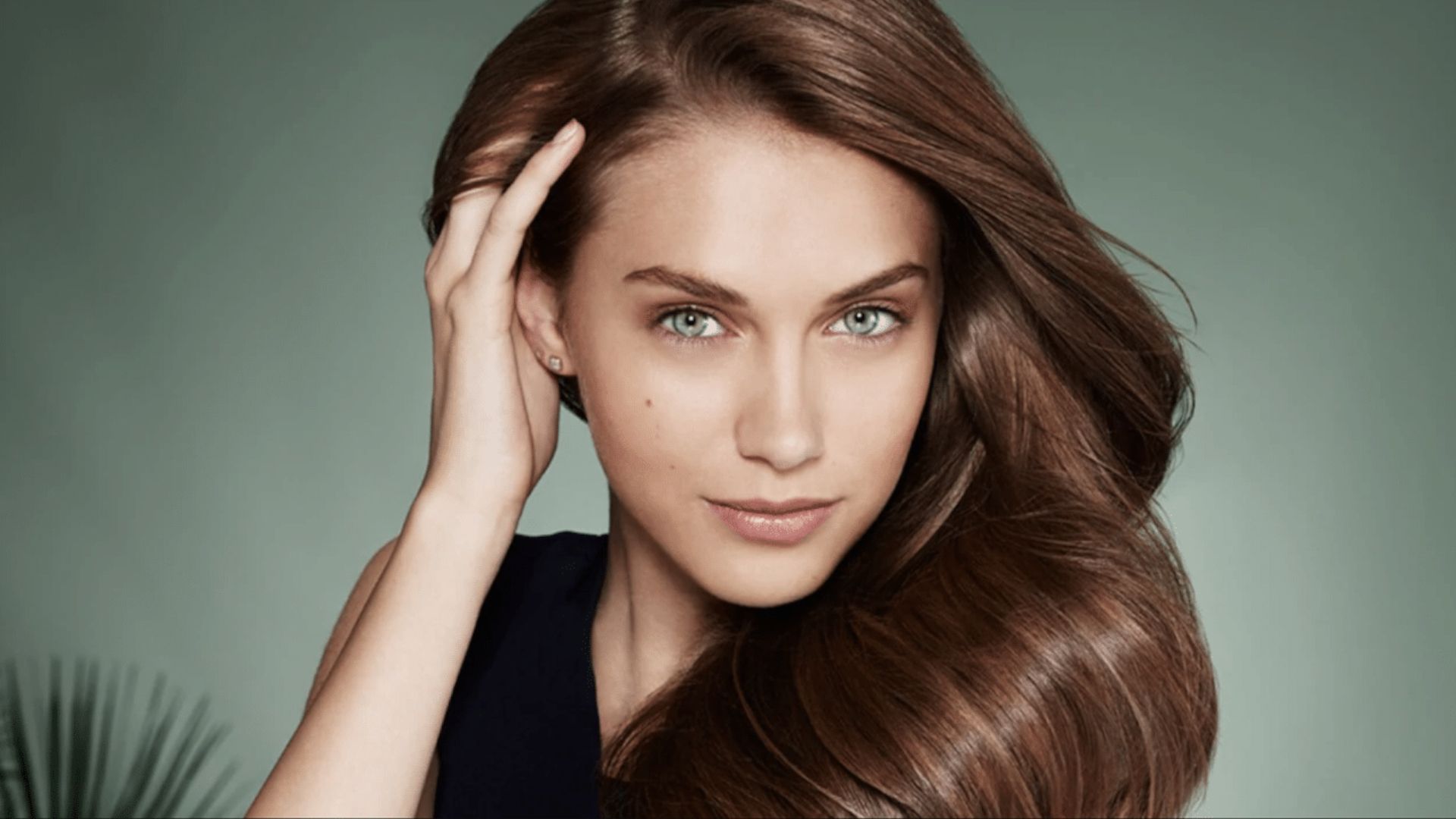 A beautiful woman is facing the camera, with her hand slowly lifting the right side of her hair.