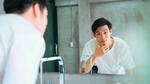 A man in a white t-shirt looking in the mirror.
