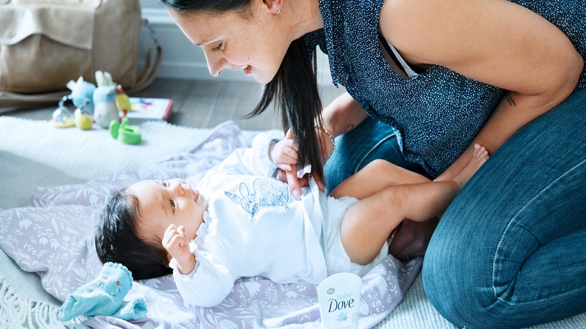 A baby is on the table with her mom holding her. She is wrapped in a towel after being bathed with Dove gentle baby products.