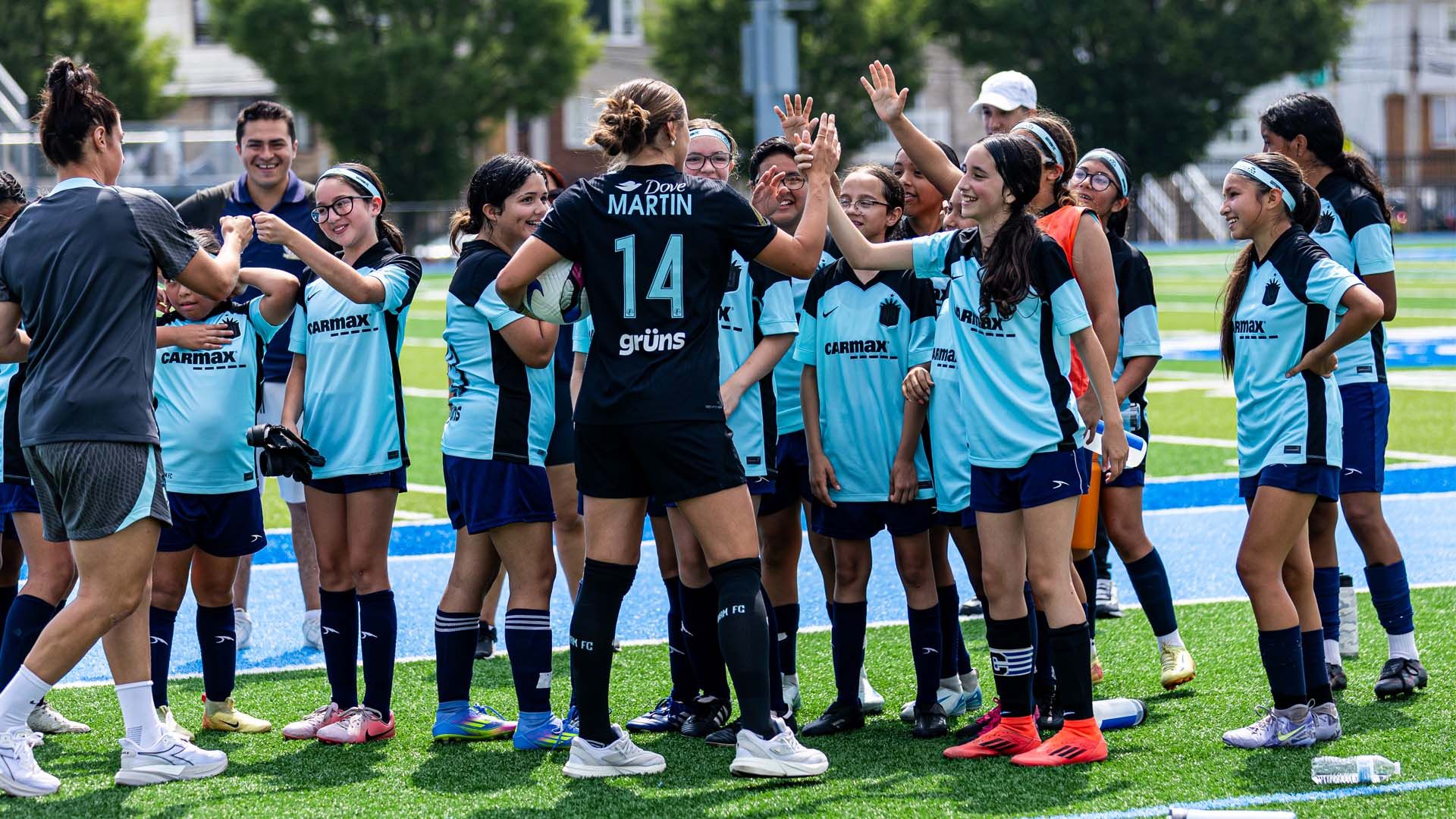 Team of smiling young girl soccer players high fiving members of the Unilever sponsored Gotham FC women’s soccer team.